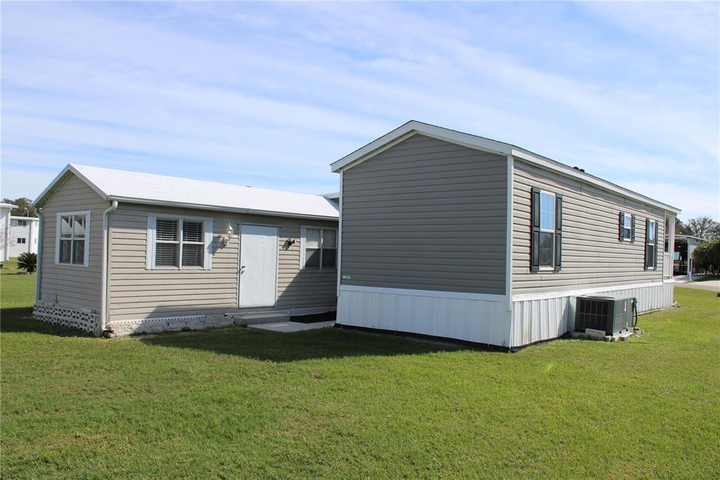 A tan mobile home with a white metal roof and gray siding sits on a lawn — 5143 NORTHSHORE DRIVE, POLK CITY, FL