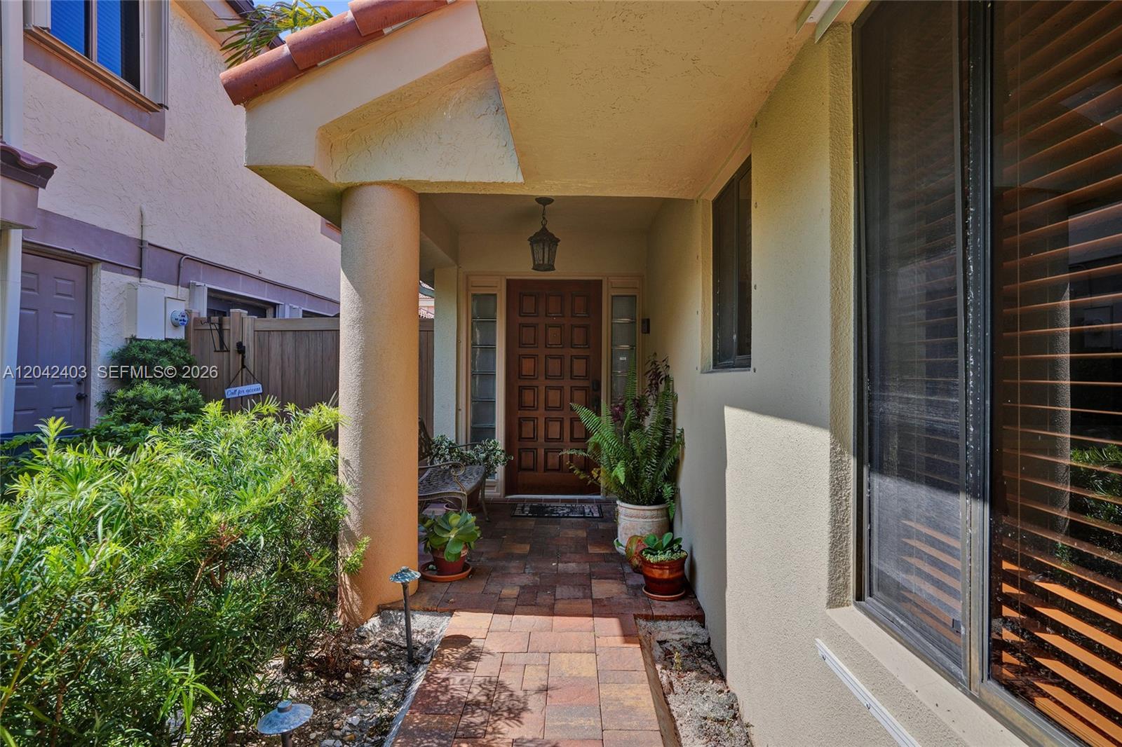 A covered entryway features a brick-paved walkway, a wooden front door, and potted plants — 9355 NW 18th Pl, Plantation FL 33322, PLANTATION, FL