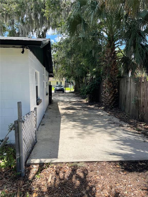 A concrete driveway runs alongside a white cinder block building toward a parked car — 1139 WOODSIDE DRIVE, DAYTONA BEACH, FL