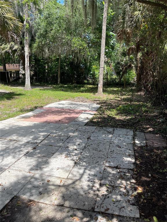 A backyard patio features light-colored square pavers and a small section of reddish-brown tiles — 1139 WOODSIDE DRIVE, DAYTONA BEACH, FL