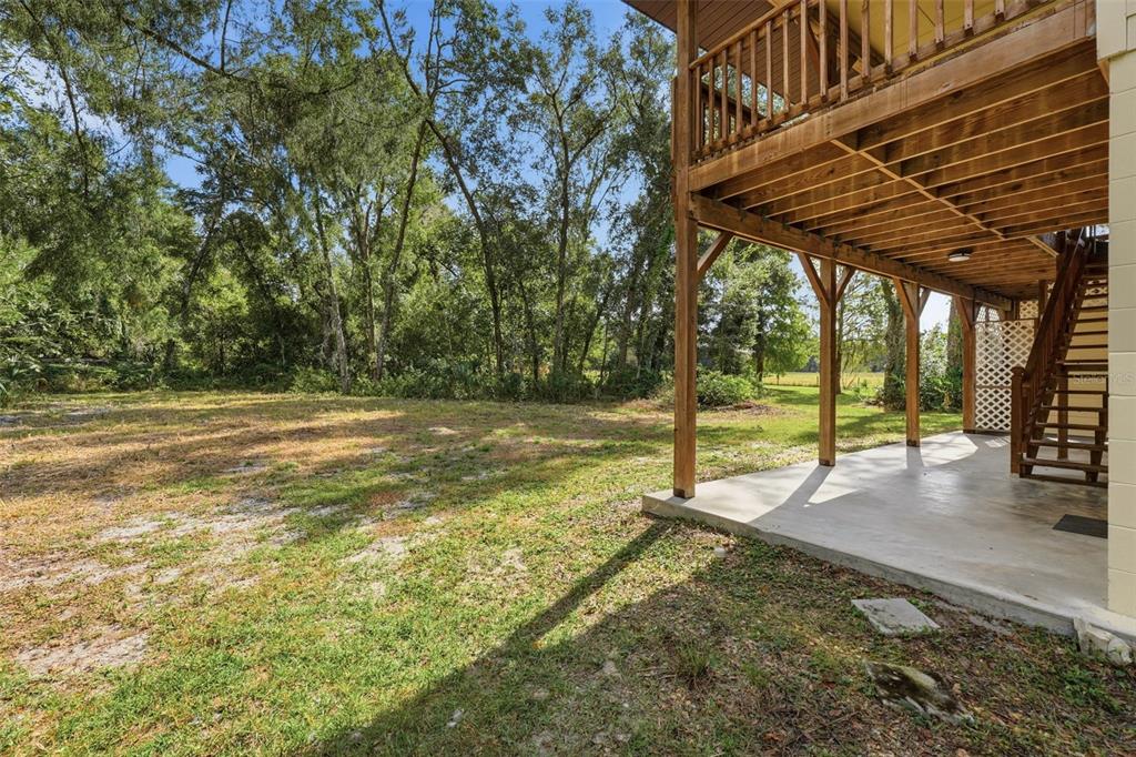 A concrete patio sits beneath a wooden deck with stairs leading to the upper level — 5505 CR 634S, BUSHNELL, FL