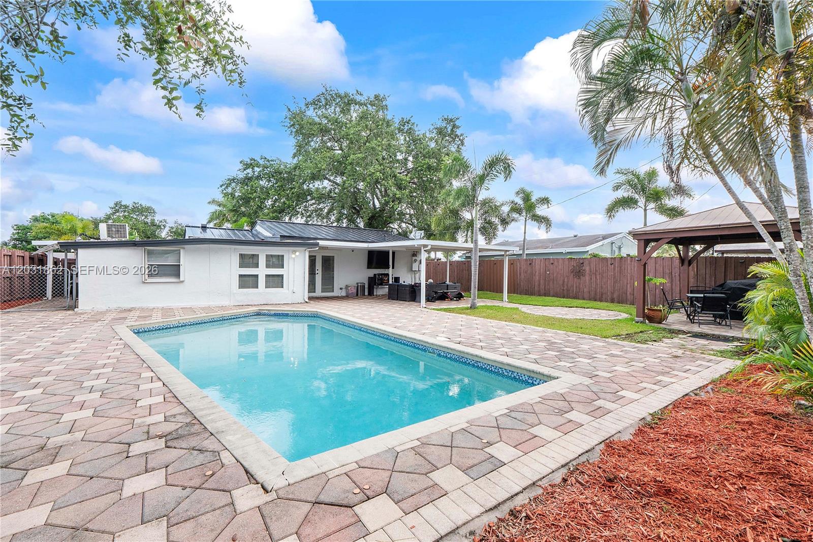A backyard features a rectangular swimming pool, a paved patio, and a wooden gazebo — 6810 Douglas St, Hollywood FL 33024, HOLLYWOOD, FL