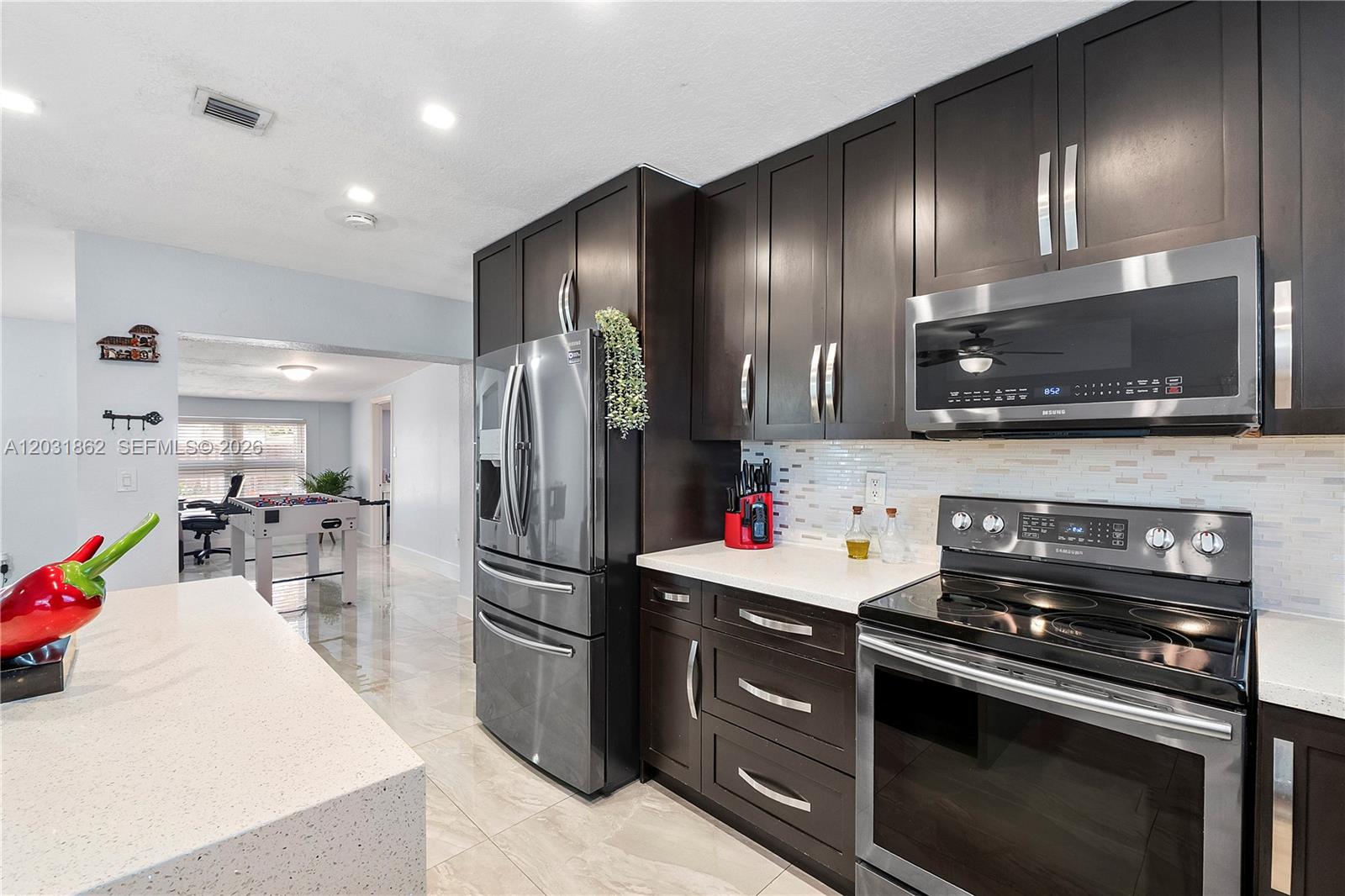 A modern kitchen features dark wood cabinets, stainless steel appliances, and light-colored quartz countertops — 6810 Douglas St, Hollywood FL 33024, HOLLYWOOD, FL