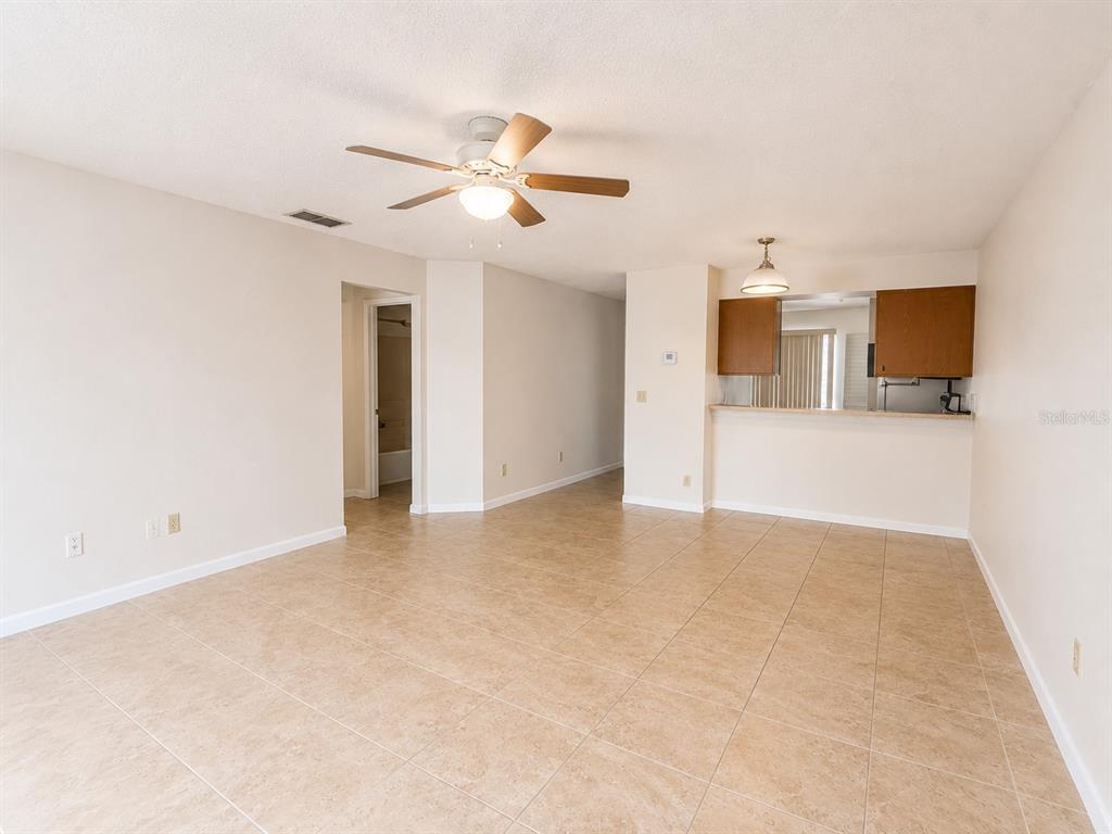 An open-concept living area features beige tile flooring, a ceiling fan, and a kitchen pass-through — 172 RESERVE CIRCLE UNIT 100, OVIEDO, FL
