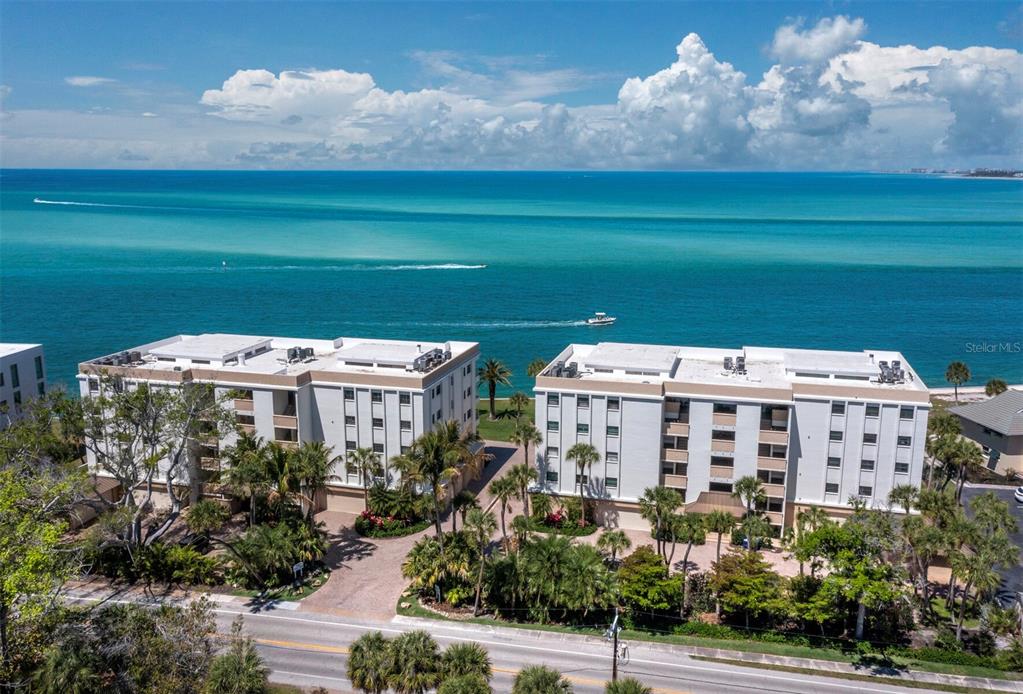 An aerial view shows two multi-story apartment buildings situated along a coastal waterfront — 4712 OCEAN BOULEVARD UNIT W10, SARASOTA, FL