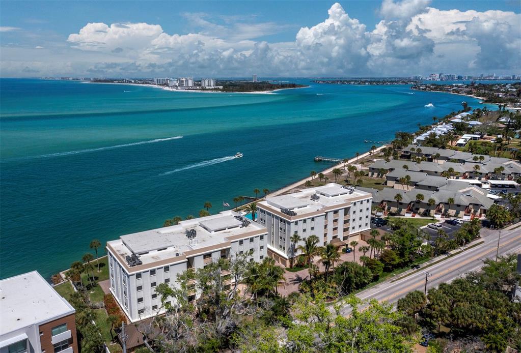 An aerial view shows waterfront apartment buildings along a coastline with a road nearby — 4712 OCEAN BOULEVARD UNIT W10, SARASOTA, FL