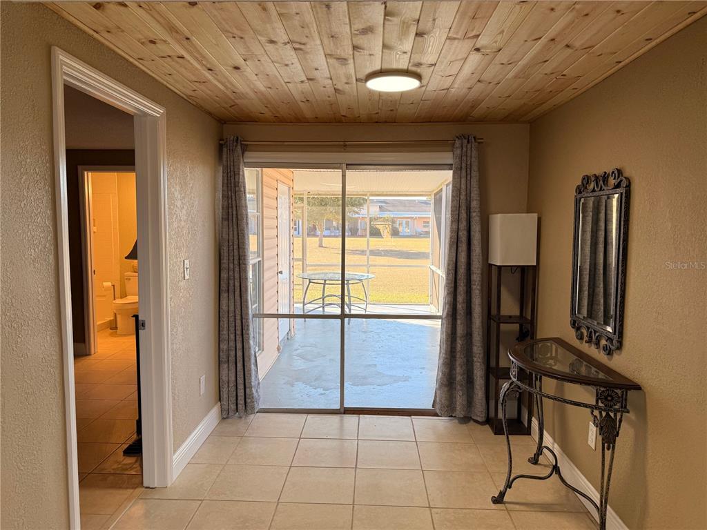 A tiled room features a wood-plank ceiling, a sliding glass door, and an adjacent bathroom — 1605 CLUB CIRCLE UNIT 1605, LAKESHORE, FL