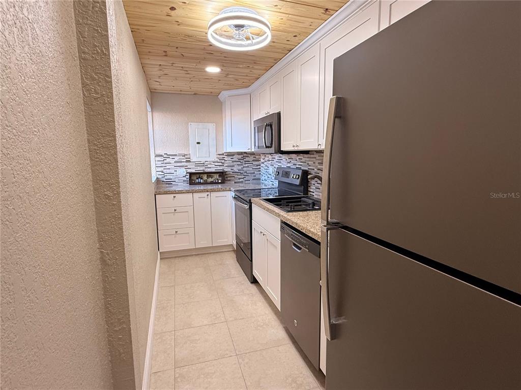 A galley kitchen features white cabinets, stainless steel appliances, tile flooring, and a wood-plank ceiling — 1605 CLUB CIRCLE UNIT 1605, LAKESHORE, FL