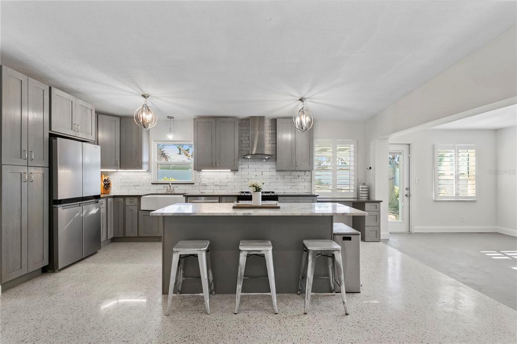A modern kitchen features gray cabinetry, a marble-topped island with three stools, and terrazzo flooring — 6931 GRANDE VISTA WAY S, ST PETERSBURG, FL