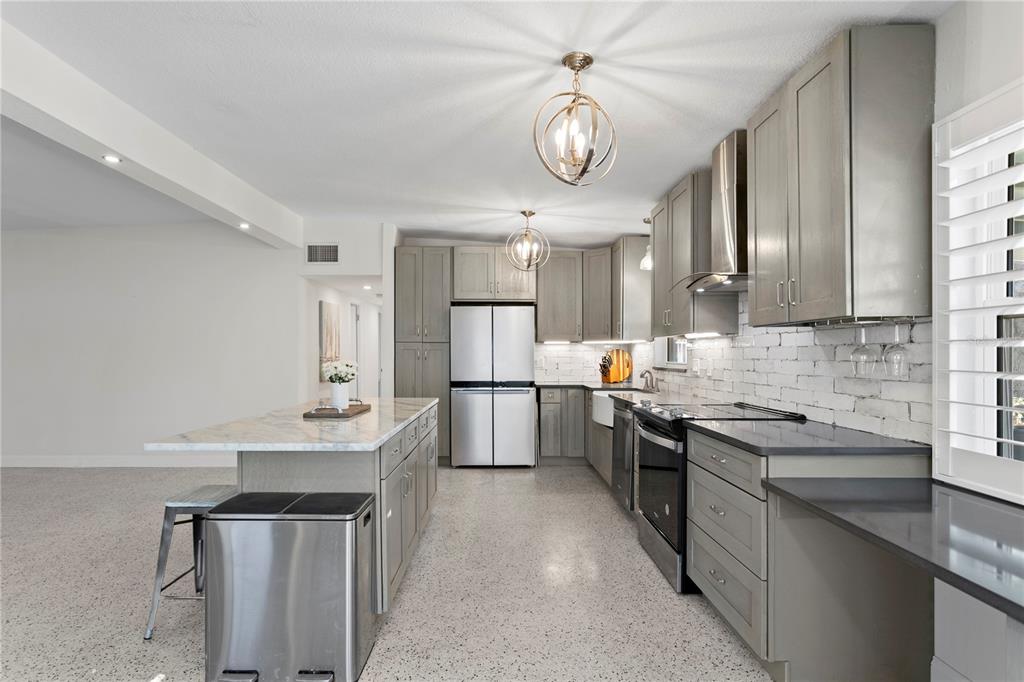 A modern kitchen features gray cabinets, a marble-topped island, stainless steel appliances, and terrazzo flooring — 6931 GRANDE VISTA WAY S, ST PETERSBURG, FL