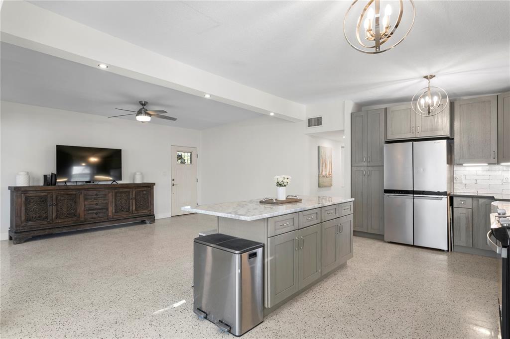 An open-concept kitchen and living area features gray cabinetry, a marble-topped island, and terrazzo flooring — 6931 GRANDE VISTA WAY S, ST PETERSBURG, FL