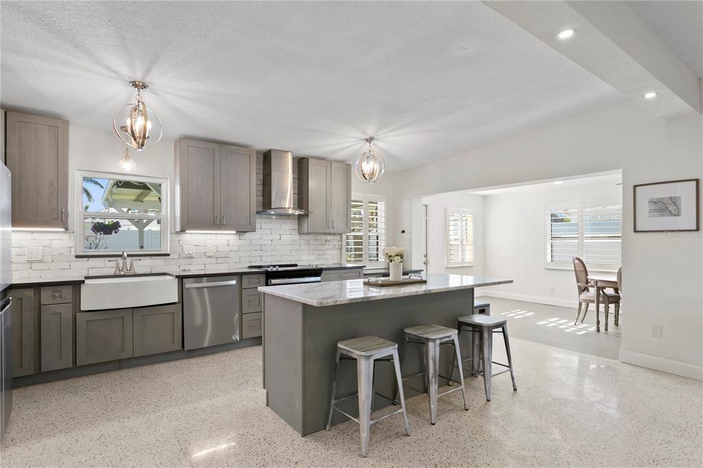 A modern kitchen features gray cabinets, a marble-topped island with stools, and white brick backsplash — 6931 GRANDE VISTA WAY S, ST PETERSBURG, FL