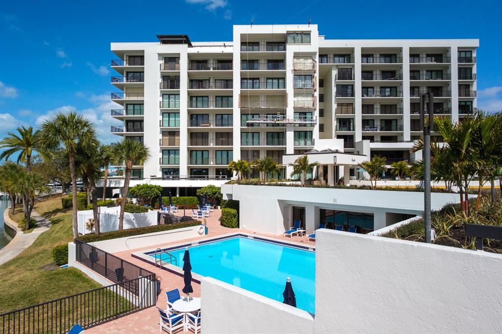 A multi-story white apartment building with a swimming pool and palm trees in the foreground — 8 BELLEVIEW BOULEVARD UNIT 108, BELLEAIR, FL