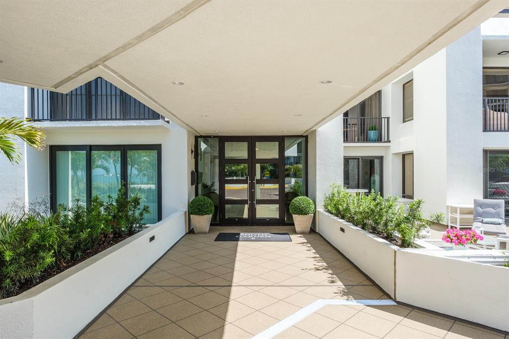 The exterior entrance features a covered walkway leading to glass double doors with potted shrubs — 8 BELLEVIEW BOULEVARD UNIT 108, BELLEAIR, FL