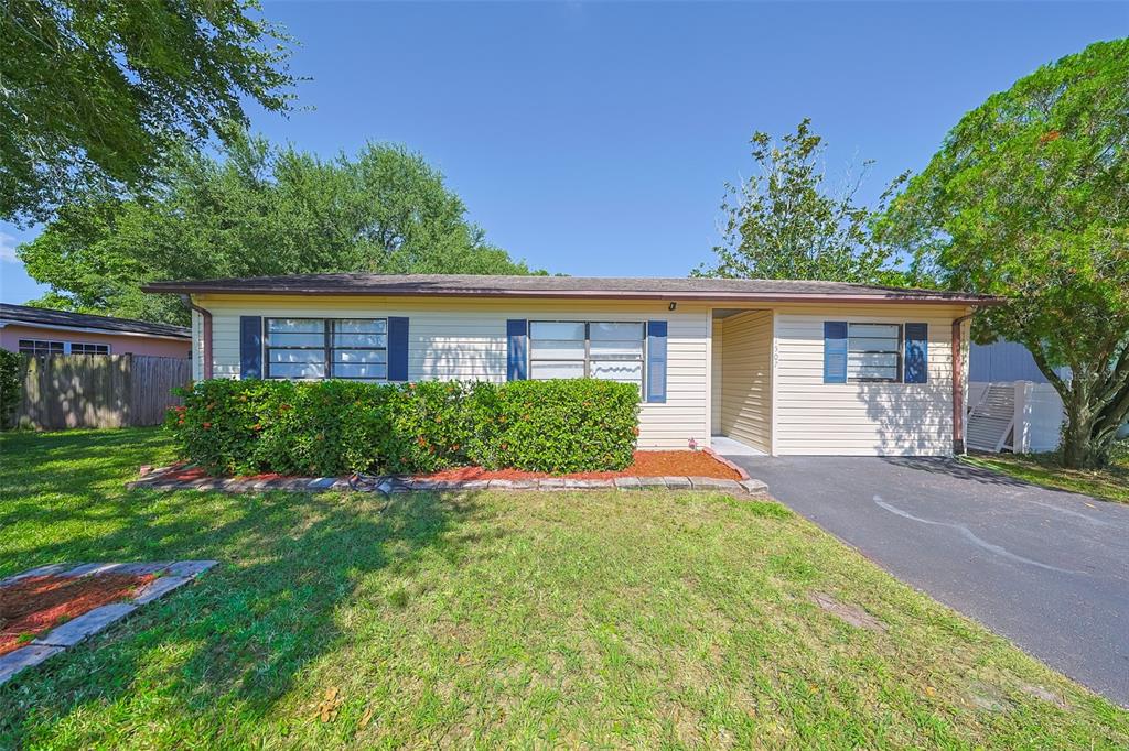 A single-story house with beige siding, blue shutters, a front hedge, and a paved driveway — 1507 76TH AVENUE N, ST PETERSBURG, FL