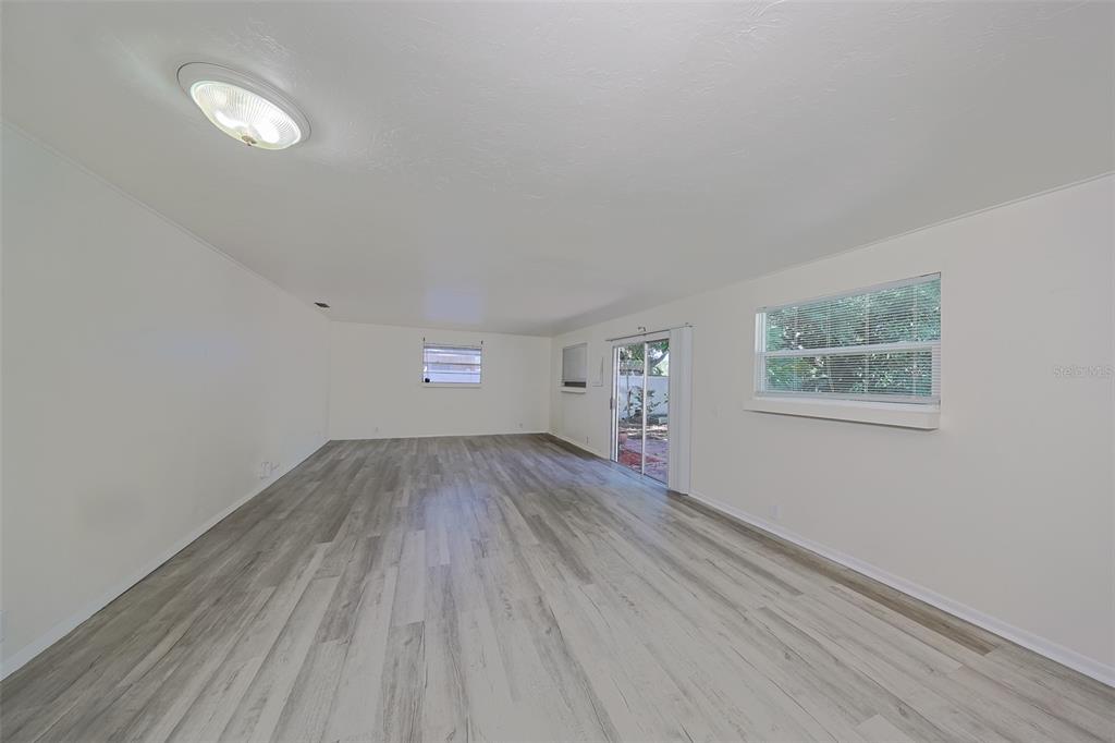 An empty room with white walls, light wood-look flooring, a ceiling light, and sliding doors — 1507 76TH AVENUE N, ST PETERSBURG, FL