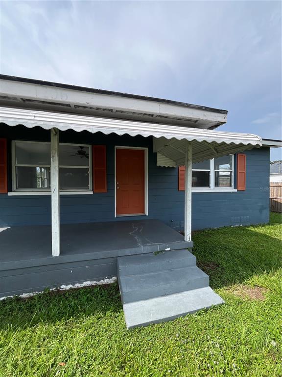 A blue house exterior features a covered porch, an orange front door, and red shutters — 1206 E CANAL STREET, MULBERRY, FL