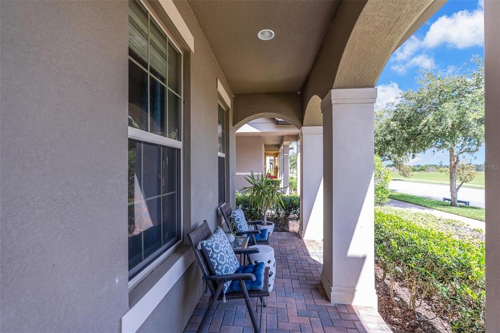 A covered outdoor patio features brick pavers, two chairs with blue cushions, and arched columns — 14230 MURCOTT BLOSSOM BOULEVARD, WINTER GARDEN, FL