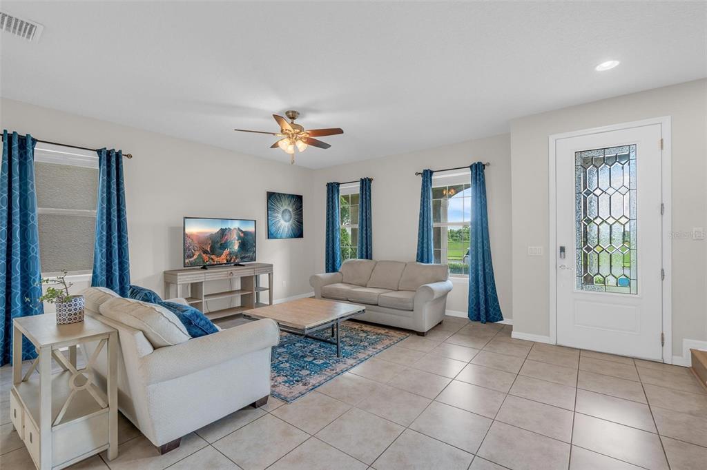 A living room features tile floors, a beige sofa, a television, and a front door — 14230 MURCOTT BLOSSOM BOULEVARD, WINTER GARDEN, FL