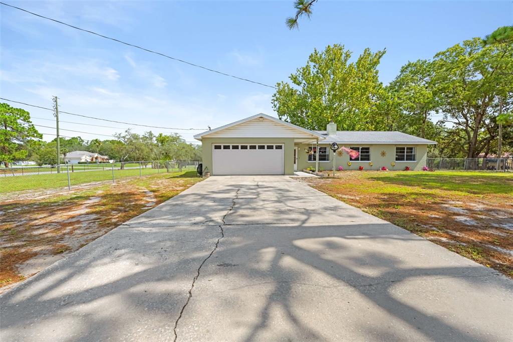 A single-story house with a white garage door and a long concrete driveway — 16517 DIPLOMAT DRIVE, SPRING HILL, FL