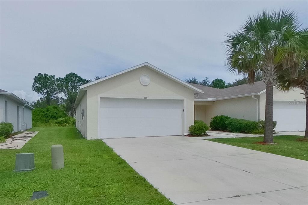 A single-story house with a white garage door, a concrete driveway, and a palm tree — 9135 AEGEAN CIRCLE, LEHIGH ACRES, FL