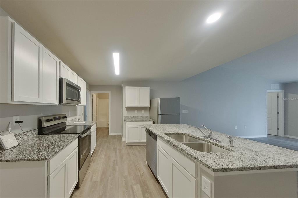 A kitchen features white cabinets, granite countertops, stainless steel appliances, and a central island — 9135 AEGEAN CIRCLE, LEHIGH ACRES, FL