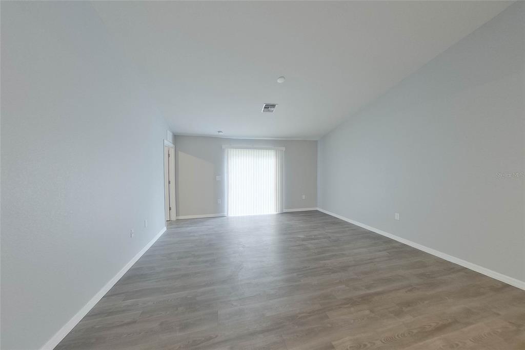 An empty living room features light gray walls, wood-look flooring, and a sliding glass door — 9135 AEGEAN CIRCLE, LEHIGH ACRES, FL