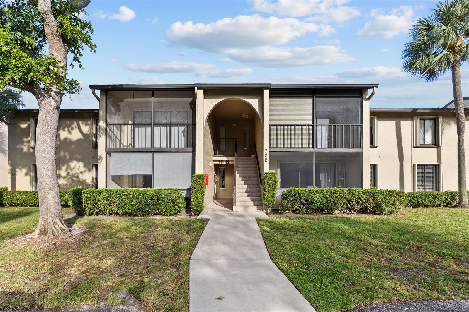 A two-story apartment building exterior features screened balconies, a central arched entryway, and stairs — 722 Sunny Pine Way # D1, FL 33415, FL
