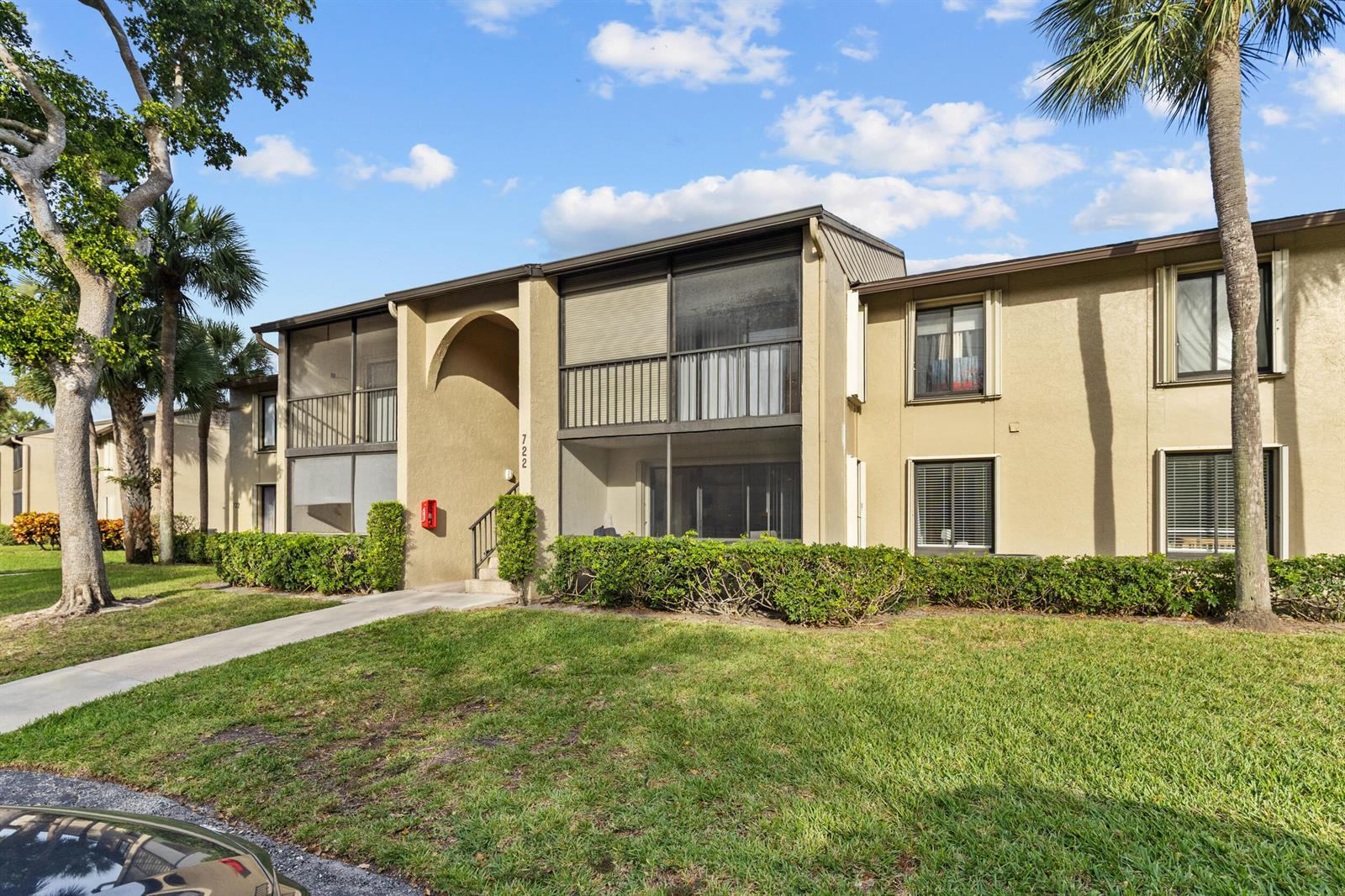 A two-story apartment building with tan stucco walls, screened balconies, and a landscaped lawn — 722 Sunny Pine Way # D1, FL 33415, FL