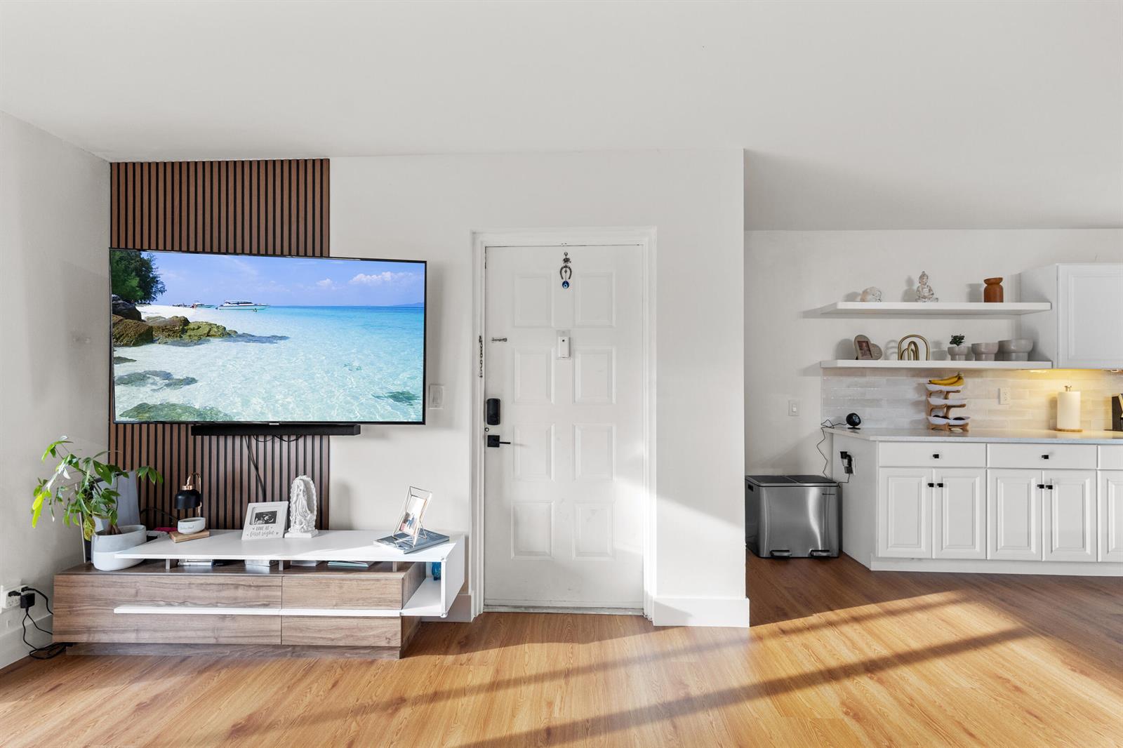 A living room features a wall-mounted television on wood slats, a white door, and kitchen — 722 Sunny Pine Way # D1, FL 33415, FL