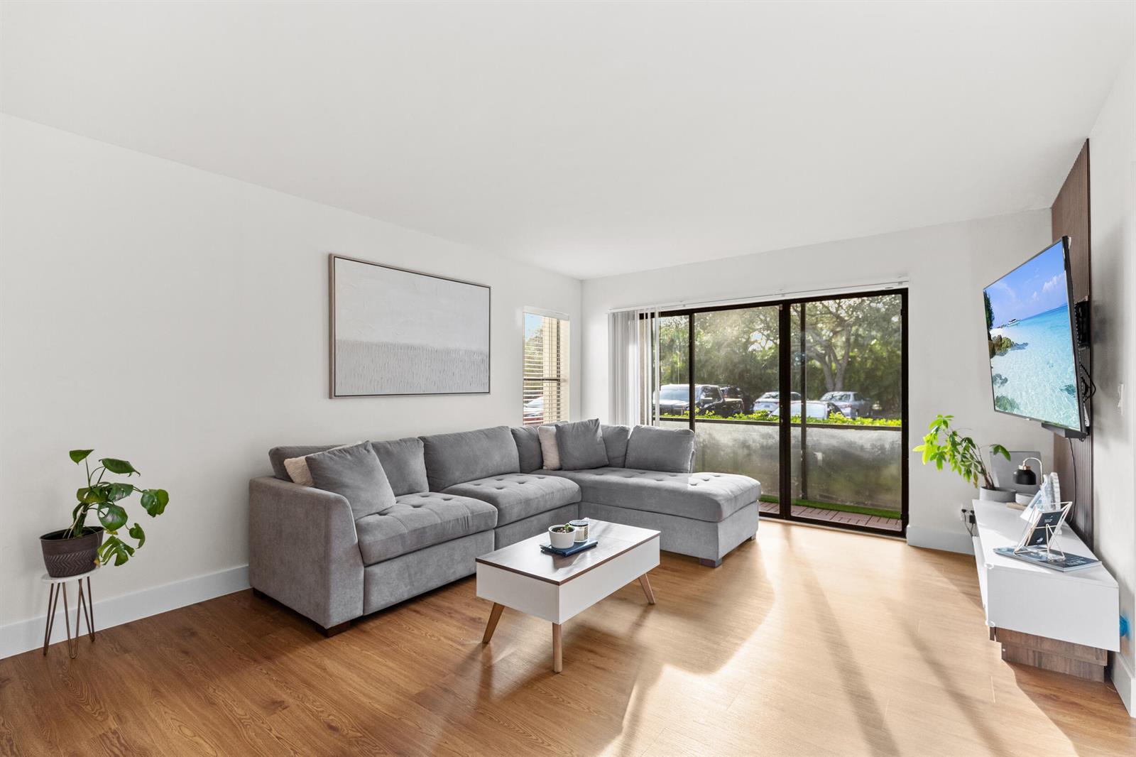 A living room features a grey sectional sofa, a coffee table, and a wall-mounted television — 722 Sunny Pine Way # D1, FL 33415, FL