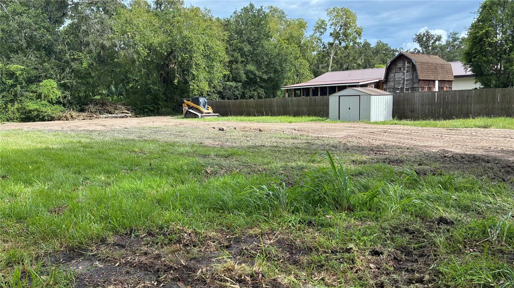 A cleared grassy lot features a small shed, a wooden fence, and a yellow skid-steer loader — 0 EAST CHERRY STREET, PLANT CITY, FL