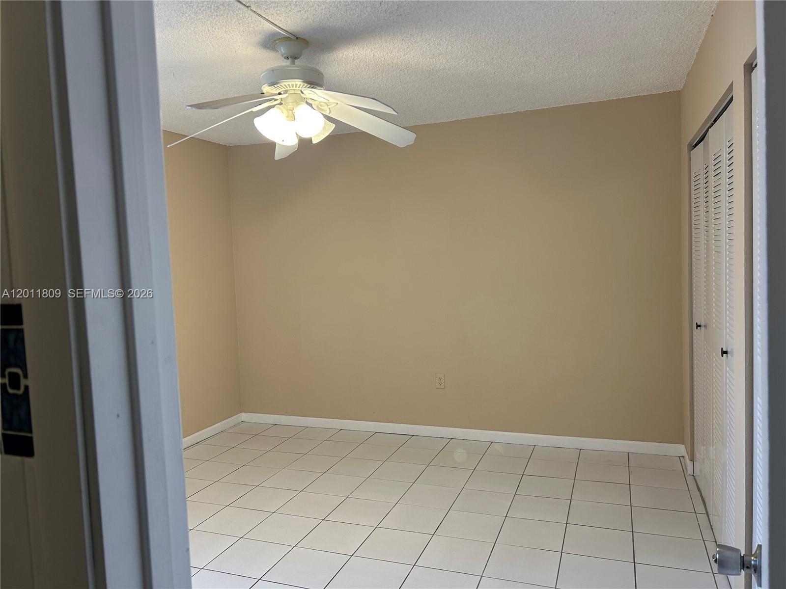 An empty bedroom features white tile flooring, beige walls, and a ceiling fan — 9411 SW 4th St # 202, Miami FL 33174, MIAMI, FL