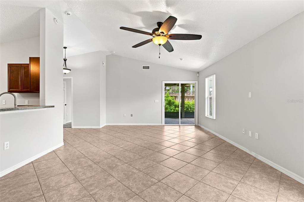 An open living area features a vaulted ceiling, tile flooring, and sliding glass patio doors — 1079 SUNSHINE WAY SW, WINTER HAVEN, FL