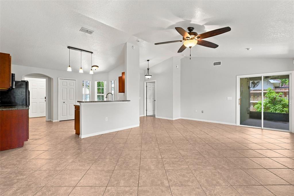 An open-concept living and kitchen area features tile flooring, a ceiling fan, and sliding doors — 1079 SUNSHINE WAY SW, WINTER HAVEN, FL