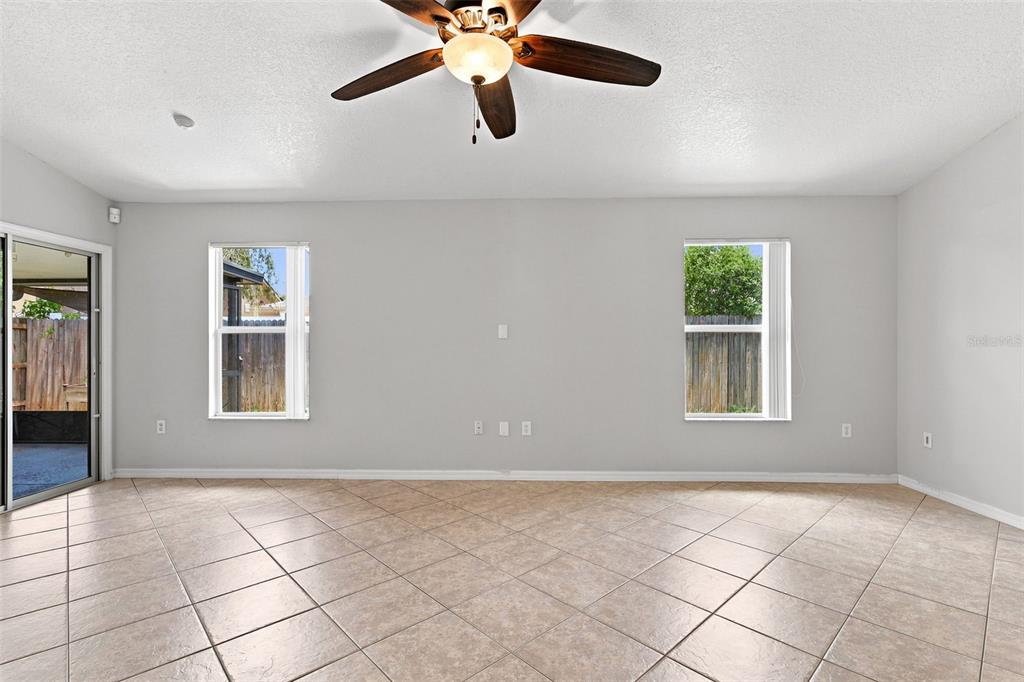 A spacious, empty living room features light tile flooring, a ceiling fan, and two windows — 1079 SUNSHINE WAY SW, WINTER HAVEN, FL