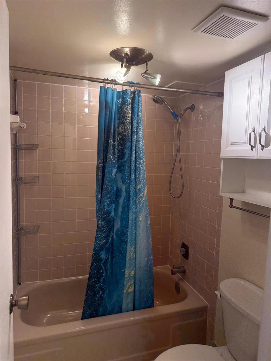 A bathroom features a tan bathtub, pink tiled walls, a blue shower curtain, and white cabinetry — 4394 NW 9th Avenue # 1a, Pompano Beach FL 33064, POMPANO BEACH, FL