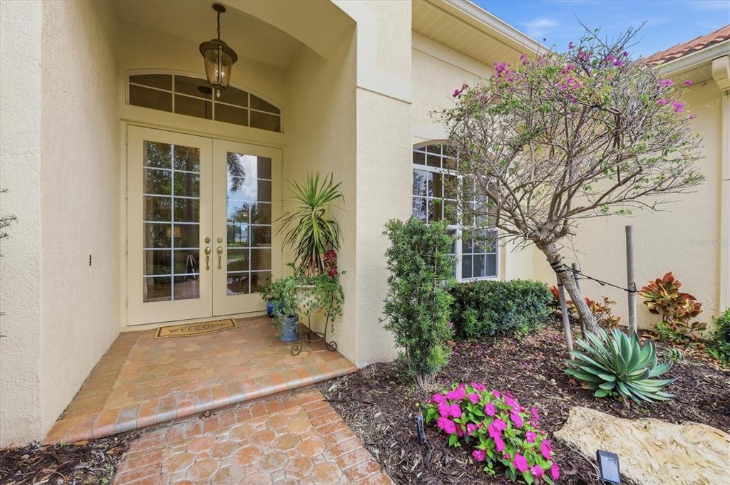 A front entryway features double glass doors, a brick walkway, and a landscaped garden bed — 1251 TUSCANY BOULEVARD, VENICE, FL