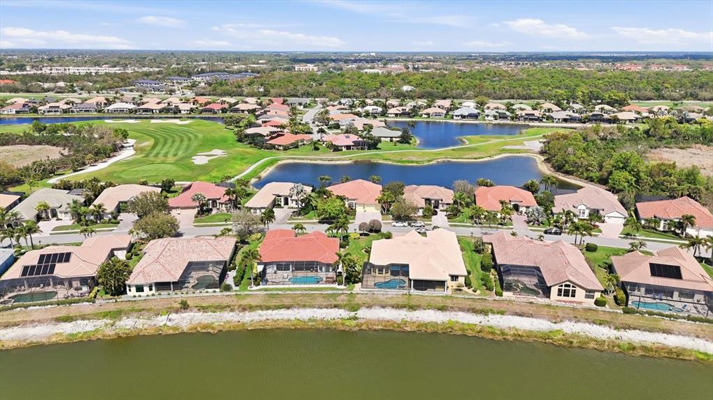 An aerial view of a residential neighborhood featuring houses with pools bordering a large lake — 1251 TUSCANY BOULEVARD, VENICE, FL