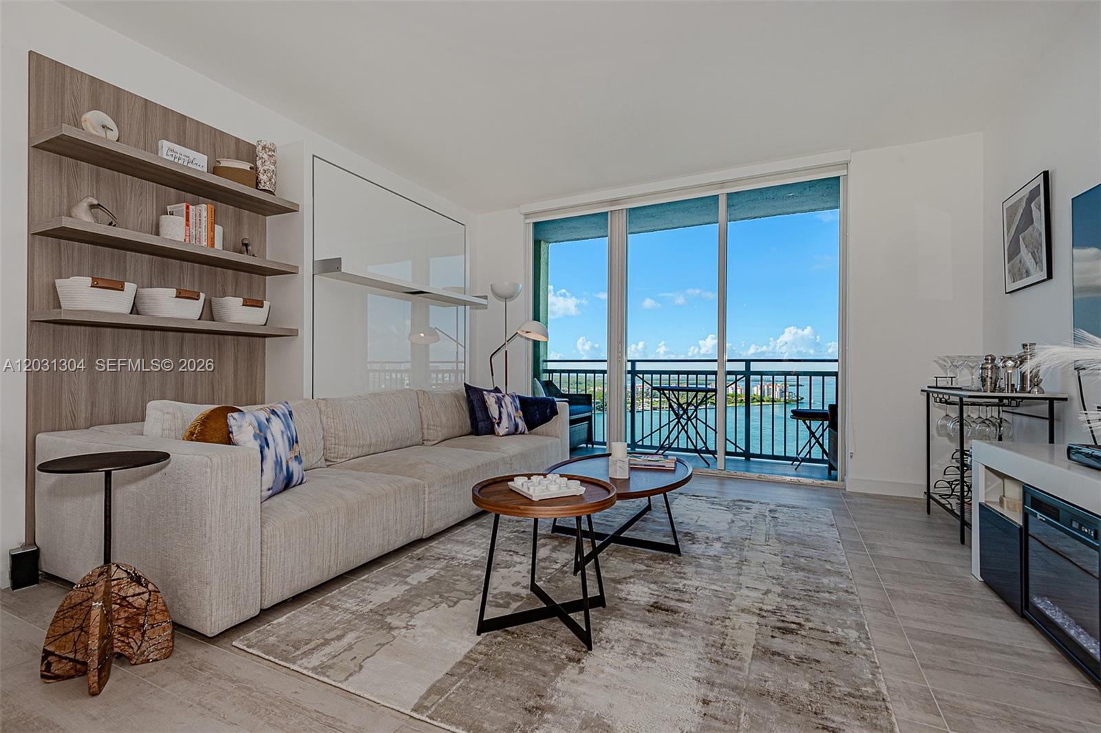 A modern living room features a sofa, nesting coffee tables, wall shelving, and a balcony view — 90 Alton Rd # 2506, Miami Beach FL 33139, MIAMI BEACH, FL