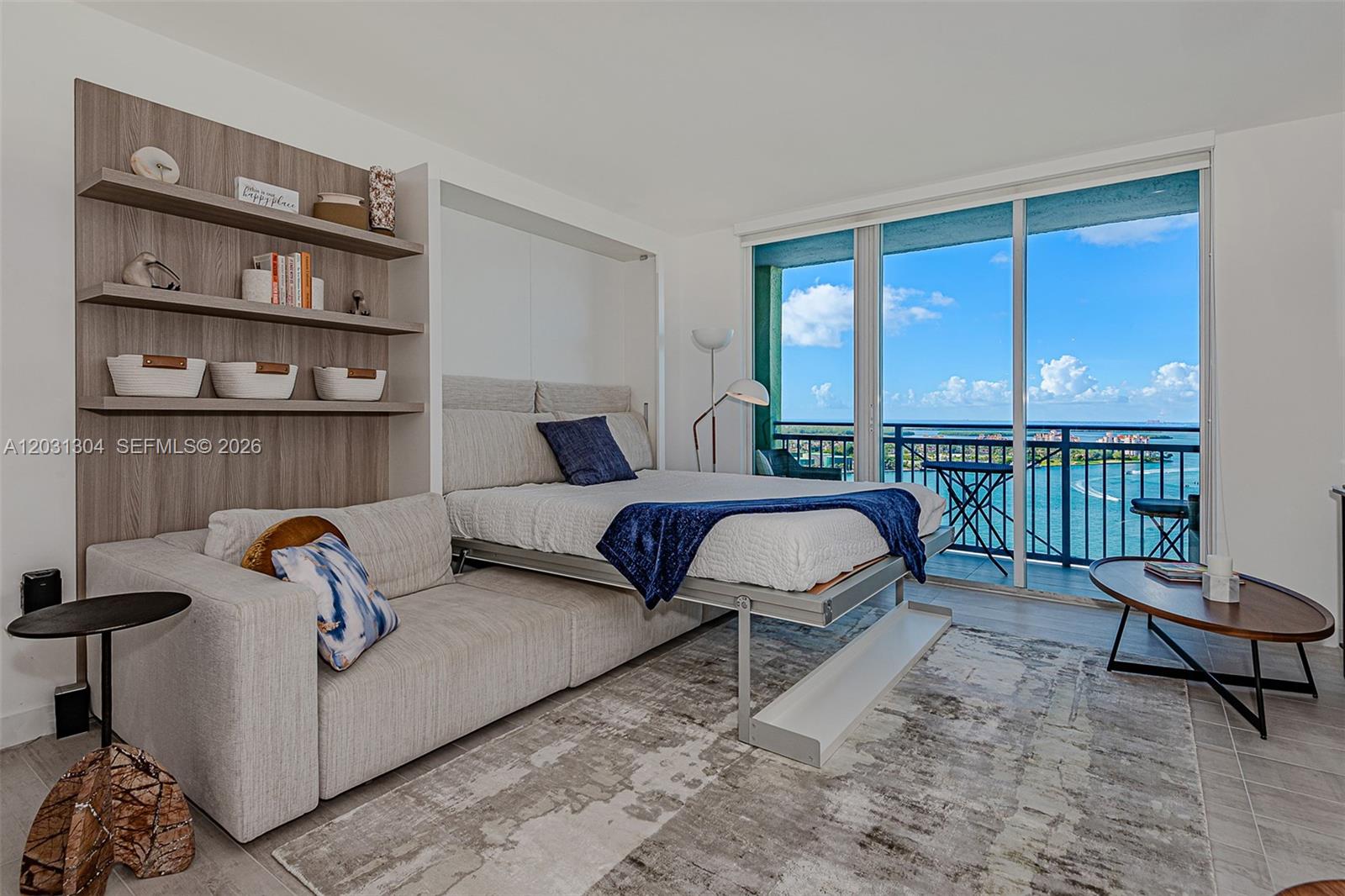 A studio apartment features a wall bed lowered over a sofa with a balcony view — 90 Alton Rd # 2506, Miami Beach FL 33139, MIAMI BEACH, FL