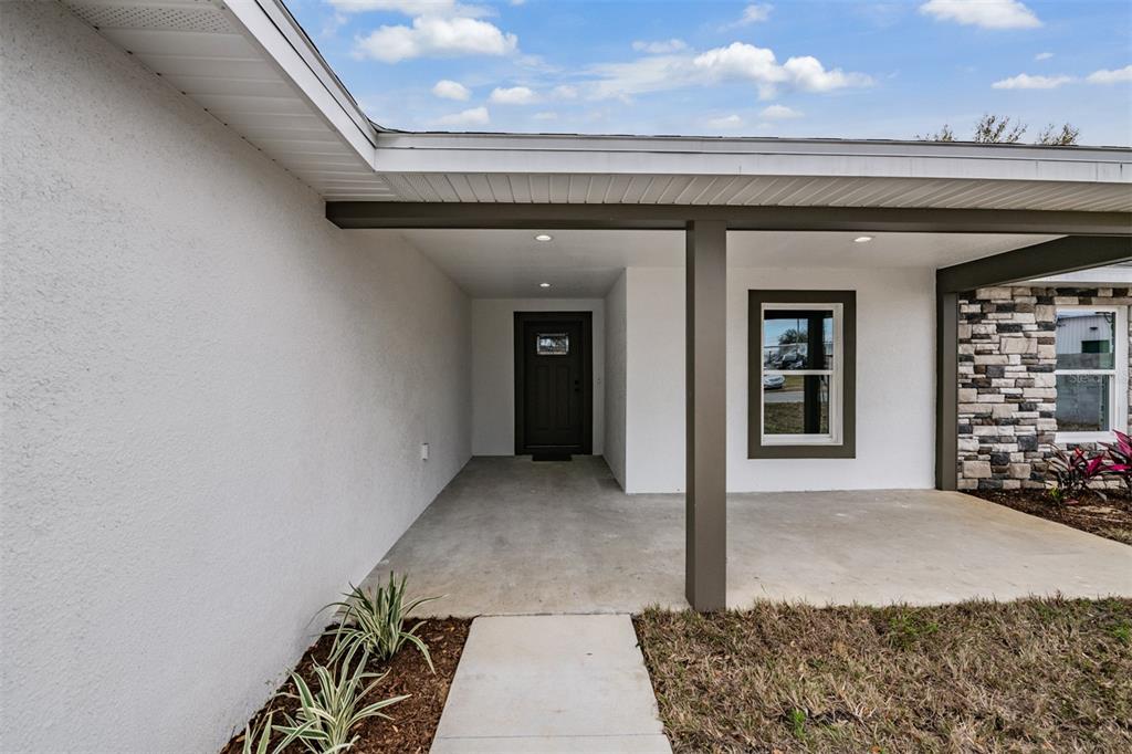A covered concrete porch leads to a dark front door beside a stone-accented exterior wall — 38086 COUNTRYSIDE PLACE, DADE CITY, FL
