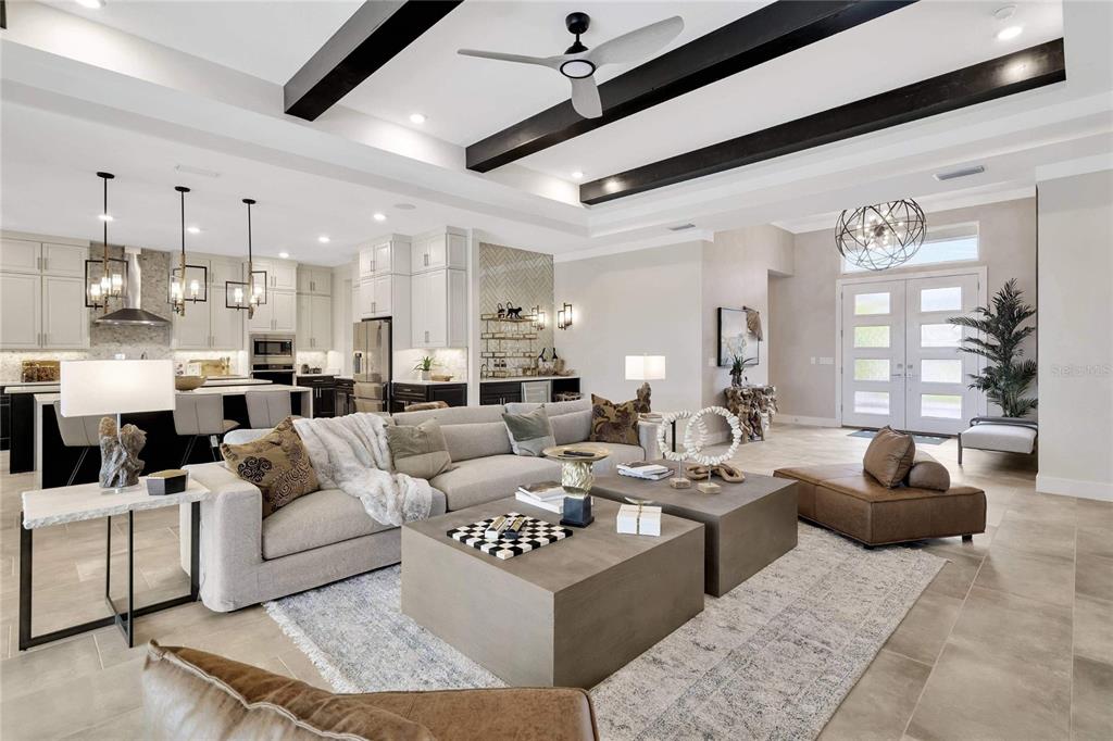 A spacious open-concept living room features a large sectional, dual coffee tables, and exposed beams — 12227 WHITE BLOSSOM COURT, PARRISH, FL