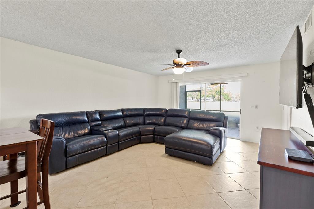 A living room features a large blue sectional sofa, tile flooring, and a sliding glass door — 6611 STONE RIVER ROAD UNIT 102, BRADENTON, FL