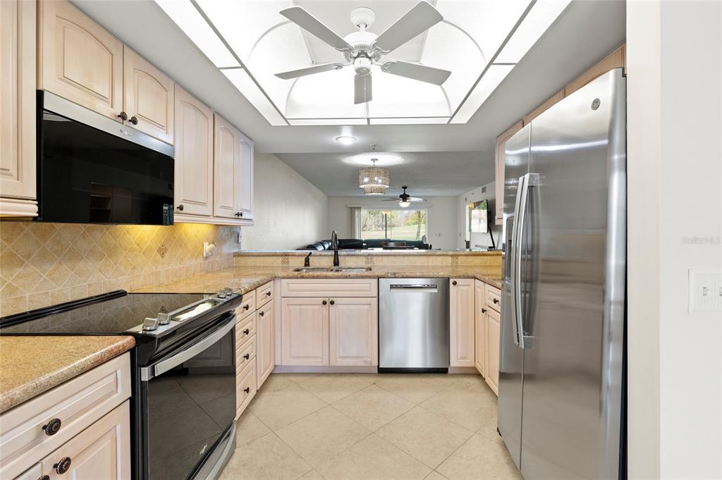 A kitchen features light wood cabinets, granite countertops, stainless steel appliances, and a ceiling fan — 6611 STONE RIVER ROAD UNIT 102, BRADENTON, FL