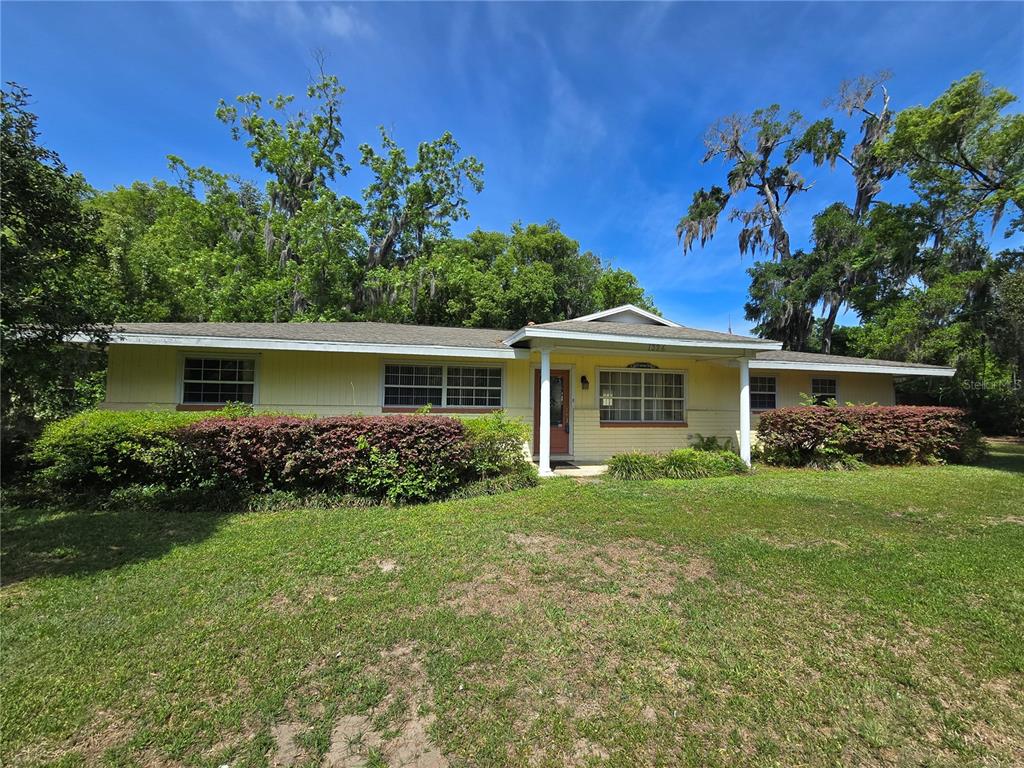 A single-story yellow house with a covered entryway is surrounded by trees and lawn — 1324 SE 33RD TERRACE, OCALA, FL