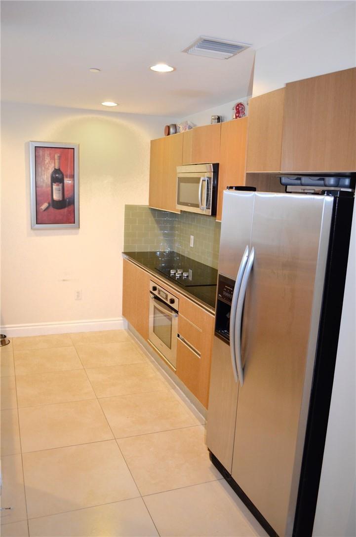 A galley kitchen features light wood cabinets, stainless steel appliances, and tan floor tiles — 1060 Brickell Avenue # 1617, Miami FL 33131, MIAMI, FL