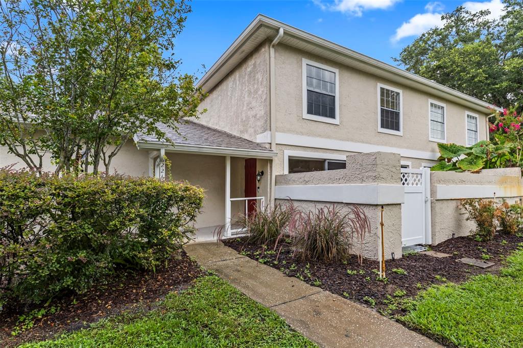A two-story townhouse exterior features a beige stucco facade, a covered entryway, and landscaping — 6226 GOLDENMOSS WAY UNIT 6226, TAMPA, FL