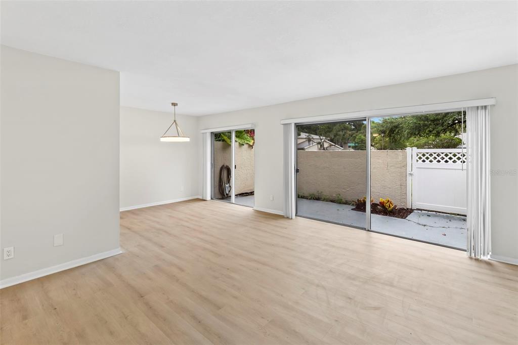 An empty living room features light wood-look flooring, white walls, and two sliding glass doors — 6226 GOLDENMOSS WAY UNIT 6226, TAMPA, FL