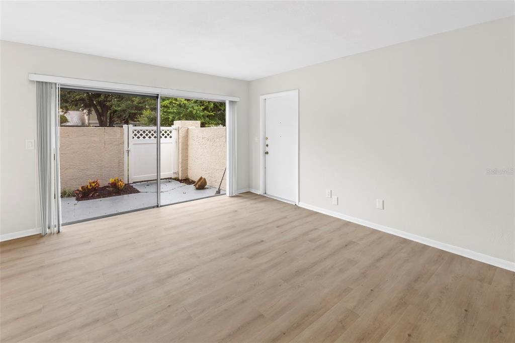 An empty living room with light wood-look flooring, a sliding glass door, and a patio — 6226 GOLDENMOSS WAY UNIT 6226, TAMPA, FL